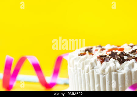 Strato di spugna torta di compleanno con panna montata di glassa di cioccolato al latte star spruzza confettura di fragole. Blu paillette potabile Nastro arricciato su giallo backg Foto Stock