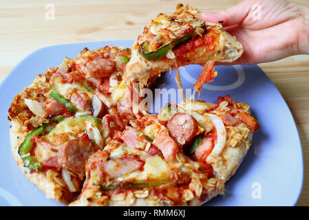 Donna raccolta a mano un pezzo di Pizza di formaggio da una piastra blu servita su un tavolo di legno Foto Stock