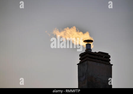 Ciminiera di un condominio impianto di riscaldamento. L'inverno raggi del sole al tramonto, il fumo del camino è colorata in giallo. Foto Stock