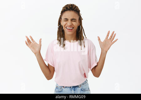 Divertito e gioioso di spensierata donna afro-americana con i timori in rosa t-shirt chiudendo gli occhi dei bracci di sollevamento con palme facce a camear sorridente con chiuso Foto Stock