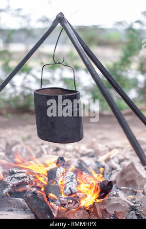 Pot turistico appesa sopra il fuoco treppiede su sfondo del fiume. Foto Stock