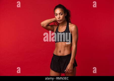 Ritratto di Ben costruita americano africano donna in nero permanente sportswear isolate su sfondo rosso Foto Stock