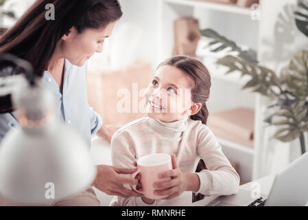 Visita della famiglia. Poco piacevole ragazza sorridente sensazione divertito mentre visitano il suo designer di moda madre presso il suo spazio in ufficio Foto Stock