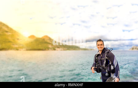 Giovane uomo bello isolato diver sorridente pronto a fare immersioni in acqua fredda muta, alette, peso belt & oxigen ingranaggio in Karaburun, Izmir. Turchia Foto Stock