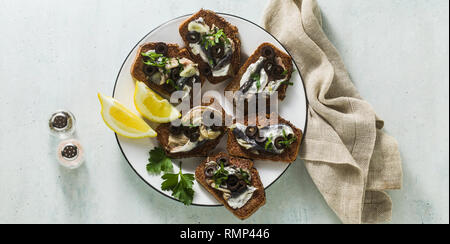 Banner di panini con Sarde marinate in olio di oliva con aglio e pane di segale. luce estiva antipasto italiano con limone e prezzemolo Foto Stock