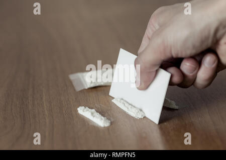Bustina di plastica, linee e la pila di cocaina su un tavolo di legno. closeup Foto Stock