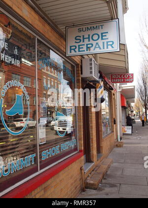 Tradizionali di piccole imprese in un bene per fare suburban area del centro cittadino. Piccole shoe repair e barbiere facendo bene. In vecchio stile barbiere polo sulla parete. Foto Stock