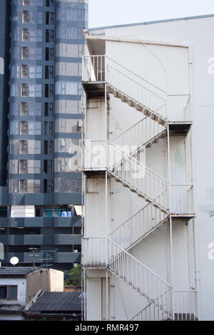 Edificio bianco a parete con scale di metallo nella parte anteriore del moderno grattacielo nero su sfondo nella città di Bangkok, Thailandia Foto Stock