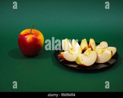 Rosso Giallo di Apple sulla piastra nera e slice isolato su sfondo verde Foto Stock