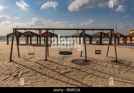 Una deserta spiaggia di sabbia di Tel Aviv, Israele, con altalene e padiglioni. Foto Stock