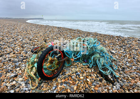 Vecchia moto aggrovigliato in una plastica rete da pesca, scartati su una spiaggia, East Sussex, Regno Unito Foto Stock