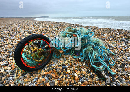 Vecchia moto aggrovigliato in una plastica rete da pesca, scartati su una spiaggia, East Sussex, Regno Unito Foto Stock