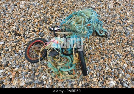 Vecchia moto aggrovigliato in una plastica rete da pesca, scartati su una spiaggia, East Sussex, Regno Unito Foto Stock