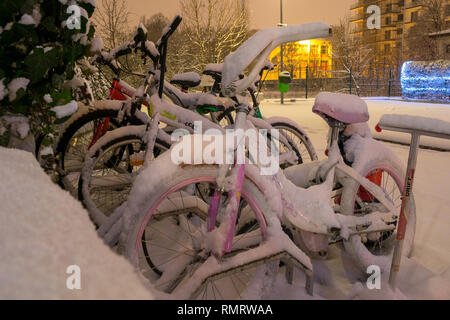 Bucarest, Romania - 7 Gennaio 2019: diversi parcheggiato biciclette da città, pesantemente coperto di neve dopo una tempesta di neve, di notte, in un palazzo di appartamenti cour Foto Stock