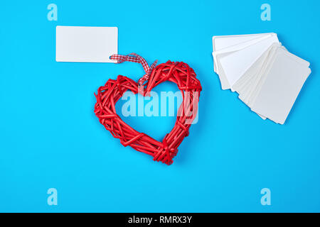 In vimini in legno cuore rosso e bianco vuoto di carta carte aziendali su sfondo blu Foto Stock