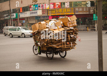 Uomo cinese a cavallo di un triciclo cargo caricato con rifiuti di cartone su una strada in Cina. Il carico di biciclette e tricicli di nolo sono popolari trasporto in Cina. X Foto Stock