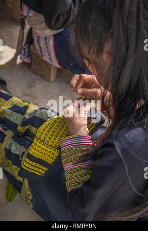 Verticale di close-up di un Rosso Dao donna creazione di tradizionali motivi di ricamo in filo giallo sul tessuto blu in Ta Phin vicino a SAPA, Vietnam. Foto Stock