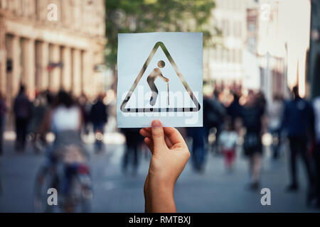 La popolazione globale invecchiamento problema. Mano che tiene un foglio di carta come un uomo vecchio con bastone su una strada affollata dello sfondo. La crescita mondiale dell'n Foto Stock