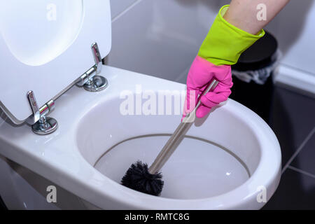 La donna in rosa guanti pulizia della tazza igienica con una spazzola per rimuovere i germi e batteri sotto il cerchio in un concetto di pulizia, igiene e hou Foto Stock