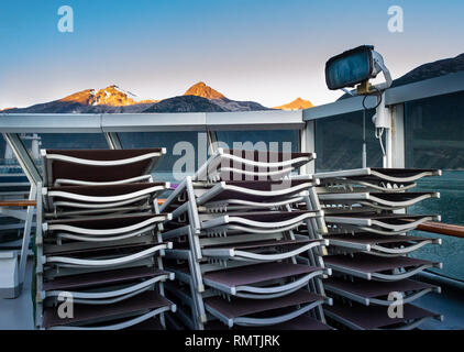 Impilati e fissati sedie a sdraio su una nave da crociera all'aperto con il ponte di mattina presto sunrise luce su sfondo montagnoso, vicino Skagway, Alaska, Stati Uniti d'America. Foto Stock