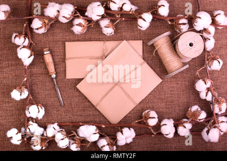 Design floreale con soffice cotone essiccato bolls e confezioni regalo su ruvida tela marrone. Vista superiore, copia spazio, biglietto di auguri Foto Stock