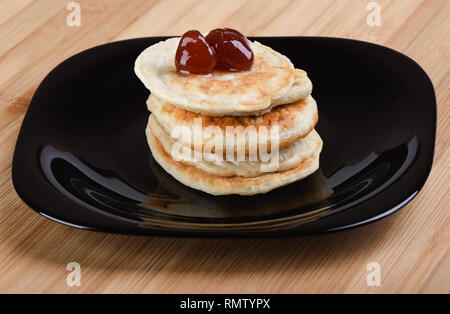 Oat pancake con fragole da jam sulla parte superiore su una piastra nera.. Sfondo di legno Foto Stock