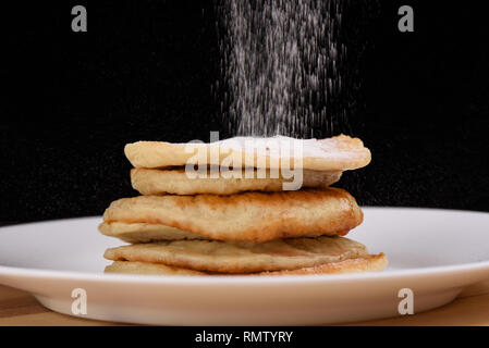Cospargere le OAT pancake con zucchero a velo. Piastra di colore bianco su uno sfondo di legno. Sfondo nero. Spazio di copia Foto Stock