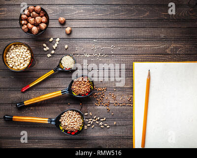 Cucchiai di legno verniciato con ornamenti floreali nello stile di Khokhloma russo arte del legno con prodotti dei settori dei cereali e del dado sul tavolo. Spazio per il tex non Foto Stock