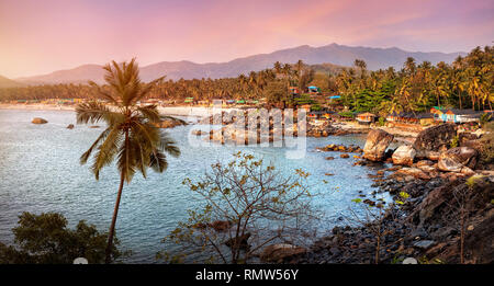 Bella vista panoramica del tramonto tropicale spiaggia con bungalow e palme di cocco a Palolem in Goa, India Foto Stock