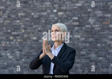 Pregando la donna con le mani giunte alla ricerca fino al cielo Foto Stock