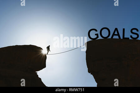 La silhouette di un uomo a piedi di bilanciamento sulla corda per obiettivi. Obiettivo di vita, di ottenere il concetto di obiettivo Foto Stock