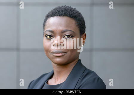 A pelo corto abbastanza nero donna in business usura, guardando la fotocamera con calma emotionless faccia in mezzo giro a busto ritratto Foto Stock