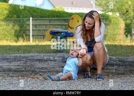 Travagliato ha sottolineato giovane madre con il suo pianto infelice figlio bambino all'aperto in un parco giochi Foto Stock