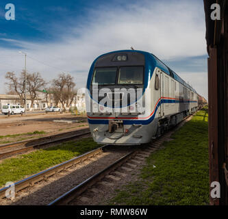 Il moderno treno in movimento su rotaie verso un punto di destinazione su uno sfondo di colore blu cielo nuvoloso. Foto Stock