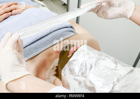 Estetista lavoratore mette un foglio di alluminio sul cliente femmina faccia, procedura dopo l'applicazione di cosmetici per il viso maschera di mare ​​algae anti trattamenti di invecchiamento Foto Stock