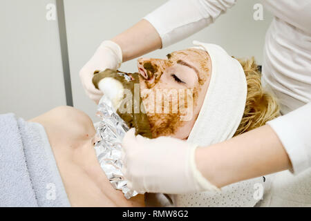 Estetista lavoratore rimozione cosmetica maschera facciale di mare ​​algae per anti invecchiamento e idratazione della pelle dal client femmina nel salone di bellezza close up Foto Stock