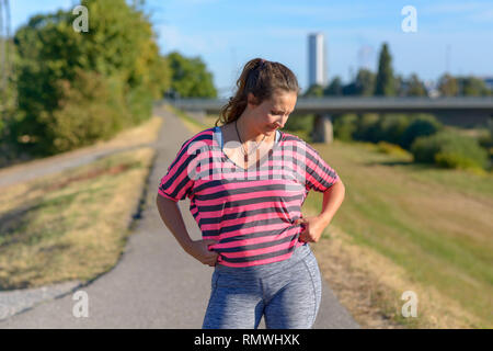 Ritratto di un giovane arrabbiato donna che guarda infastidito al suo ventre grasso indossando rosa fitness top senza maniche all'aperto Foto Stock
