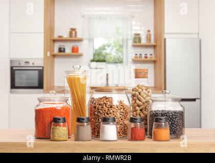 Molti vasi di vetro con diversi ingredienti e spezie su un piano di lavoro di una cucina Foto Stock