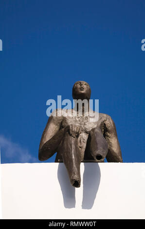 Umano maschio di scultura di metallo seduta sul bordo di un tetto, Fira, Santorini, Grecia Foto Stock