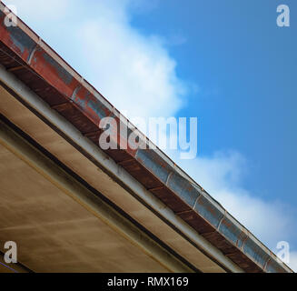 La rottura di una gronda del tetto di casa in vista dal basso, vecchie e arrugginite con cielo blu sullo sfondo. Foto Stock