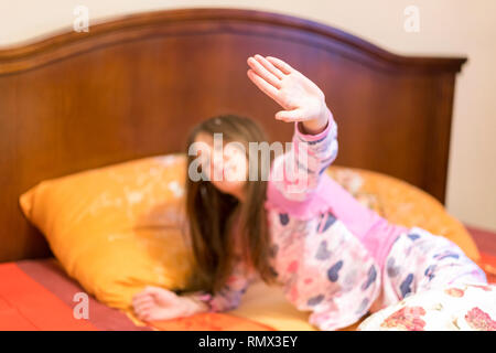 Carino bambina lo stiramento delle sue braccia felicemente con un sorriso da svegliarsi nel suo letto. bambino sbadiglia assonnato a letto. Assonnato bambina sul letto Foto Stock