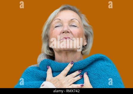 Attraente donna senior assaporando il momento in piedi con gli occhi chiusi e la testa inclinata indietro con un espressione serena come essa abbraccia il suo torace con h Foto Stock