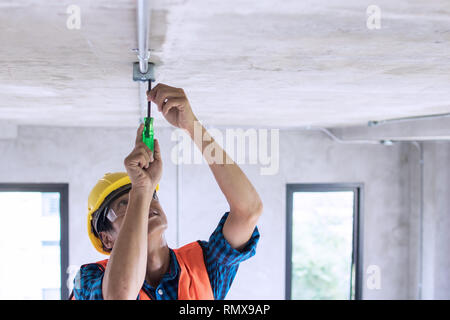 Elettricista cablaggio sul soffitto in sito in costruzione Foto Stock