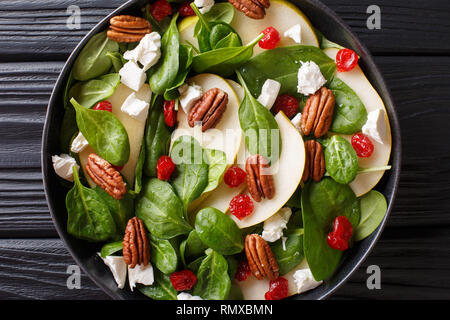 Insalata fresca di pere, gli spinaci, le noci pecan, formaggio di capra e le ciliegie secche close-up su una piastra sul tavolo. Parte superiore orizzontale vista da sopra Foto Stock