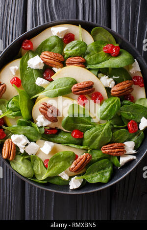 Insalata fresca di pere, gli spinaci, le noci pecan, formaggio di capra e le ciliegie secche close-up su una piastra sul tavolo. Verticale in alto vista da sopra Foto Stock