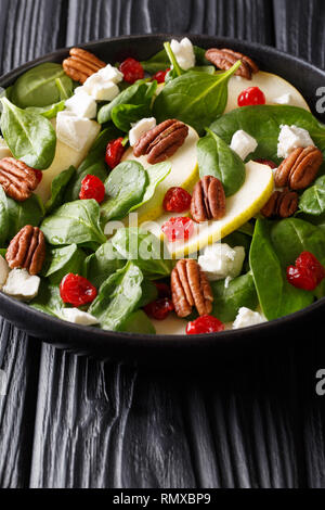 Insalata di naturale con pere fresche, verde di spinaci, le noci pecan, il formaggio feta e le ciliegie secche close-up su una piastra sul piano verticale. Foto Stock