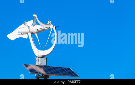 Di piccole dimensioni e di colore bianco turbina a vento solare con il pannello della batteria oltre il cielo blu sullo sfondo Foto Stock