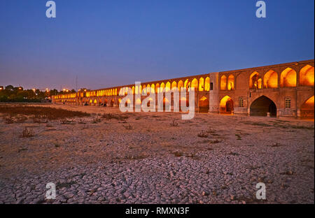 Passeggiata serale lungo la banca di essiccato fino Zayanderud fiume con una vista su illuminato storico ponte Siosepol, Isfahan, Iran. Foto Stock