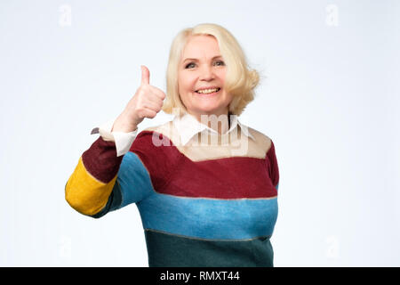 Allegro vecchia donna in felpa colorata che mostra Thumbs up gesto Foto Stock