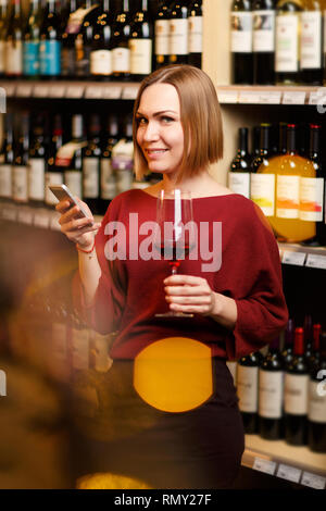 Foto del giovane biondo con un bicchiere in mano in negozio con il vino Foto Stock